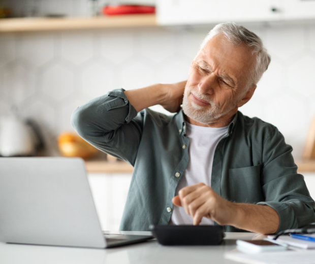 Senior man suffering neckache while working with laptop kitchen interior